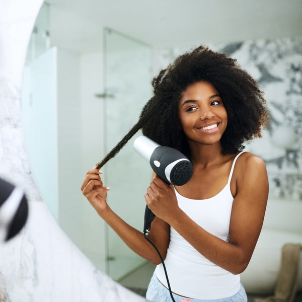 Woman drying her hair with a hair dryer in front of a mirror
